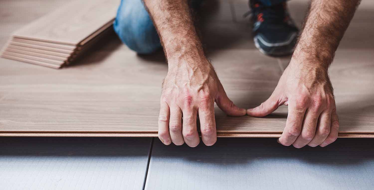 Close-up of a person installing laminate flooring, showing their hands aligning the edges of the flooring planks for a seamless fit.