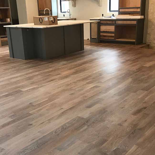 A modern kitchen with light wood flooring installed by Orange Cat Flooring in Atlanta, GA, featuring a large island and unfinished cabinetry.