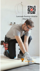 A professional flooring installer wearing safety glasses and gloves works on a laminate flooring project. The image includes a QR code, the text "Laminate flooring contractor Atlanta, GA," and Orange Cat Flooring's logo, contact information, and website.